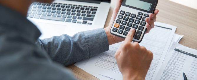 Person calculating finances with a calculator and paperwork on a desk